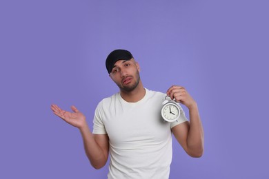 Tired man with alarm clock on violet background. Insomnia problem