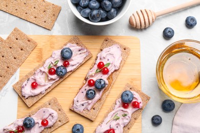 Photo of Tasty cracker sandwiches with cream cheese, blueberries, red currants, thyme and honey on grey marble table, flat lay