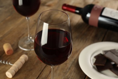 Photo of Glasses of tasty red wine and chocolate on wooden table, closeup