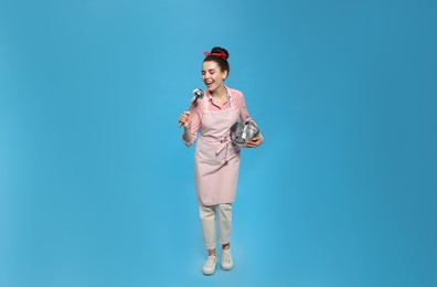 Housewife with pan and ladle on light blue background