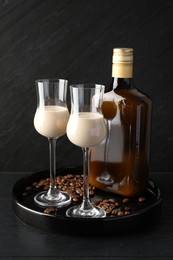 Coffee cream liqueur in glasses, bottle and beans on black wooden table