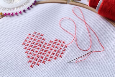 Embroidered red heart and needle on white cloth, closeup