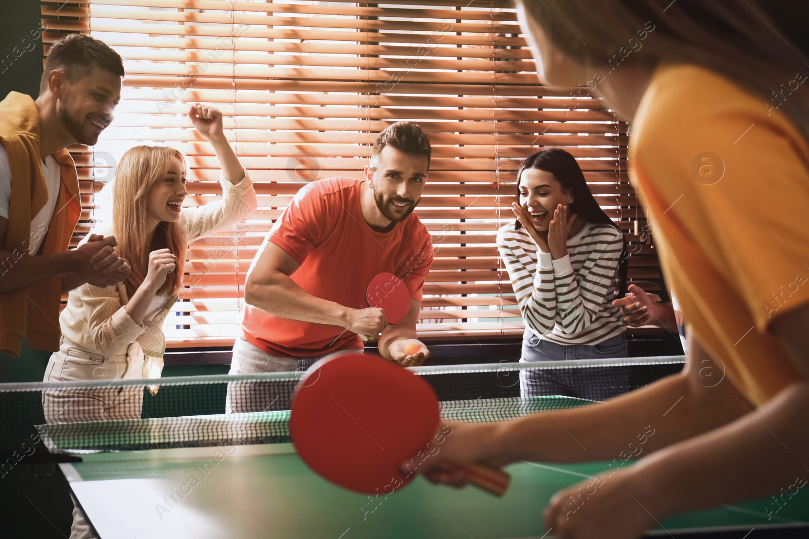 Photo of Happy friends playing ping pong together indoors