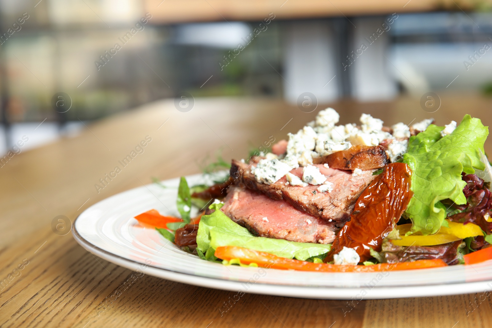 Photo of Delicious salad with roasted meat and vegetables served on wooden table indoors, closeup