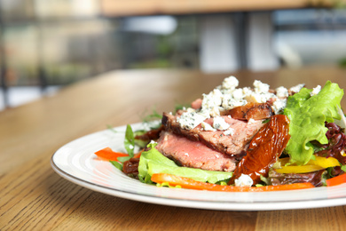 Photo of Delicious salad with roasted meat and vegetables served on wooden table indoors, closeup