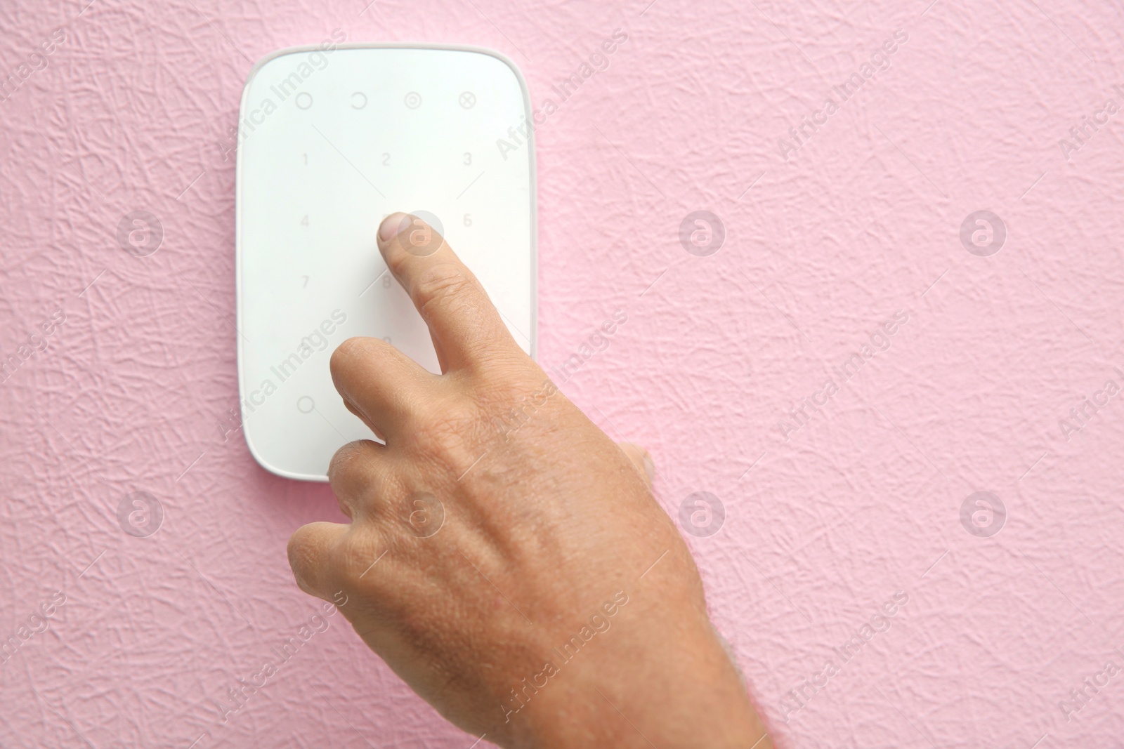 Photo of Mature man entering code on alarm system keypad indoors