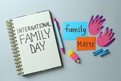 Photo of Notebook with text International Family Day May, paper hand cutouts and stationery on light grey background, flat lay
