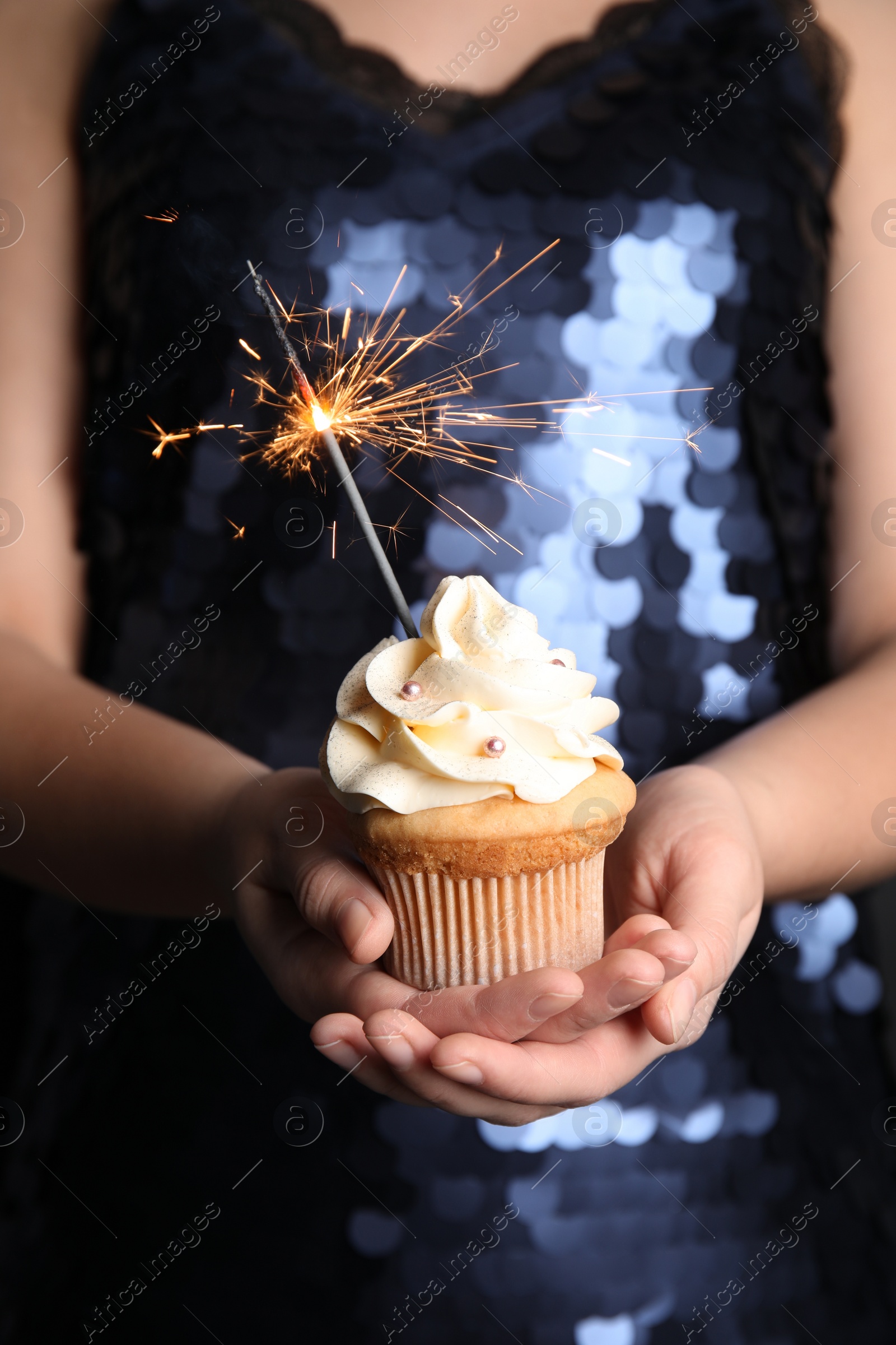 Photo of Woman holding birthday cupcake with sparkler, closeup