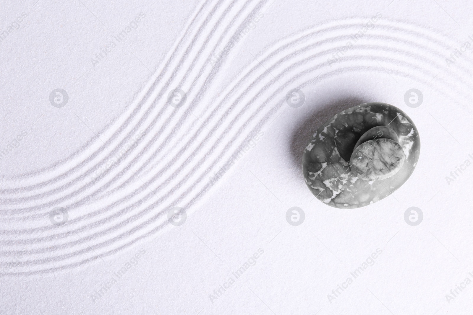 Photo of Zen garden stones on white sand with pattern, top view. Space for text