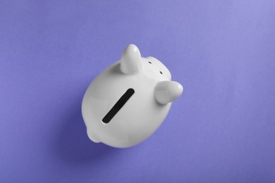 Ceramic piggy bank on violet background, top view. Financial savings