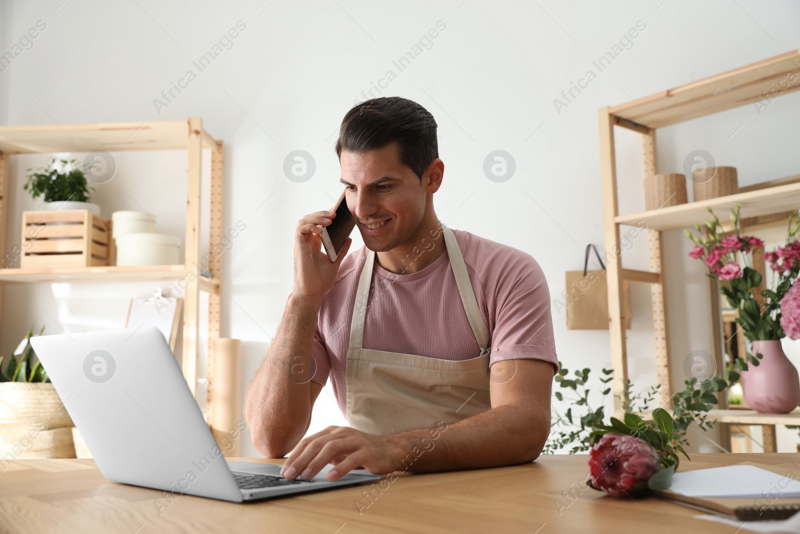 Photo of Florist talking on smartphone near laptop in workshop