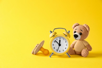Alarm clock, toy bear and baby dummy on yellow background, space for text. Time to give birth