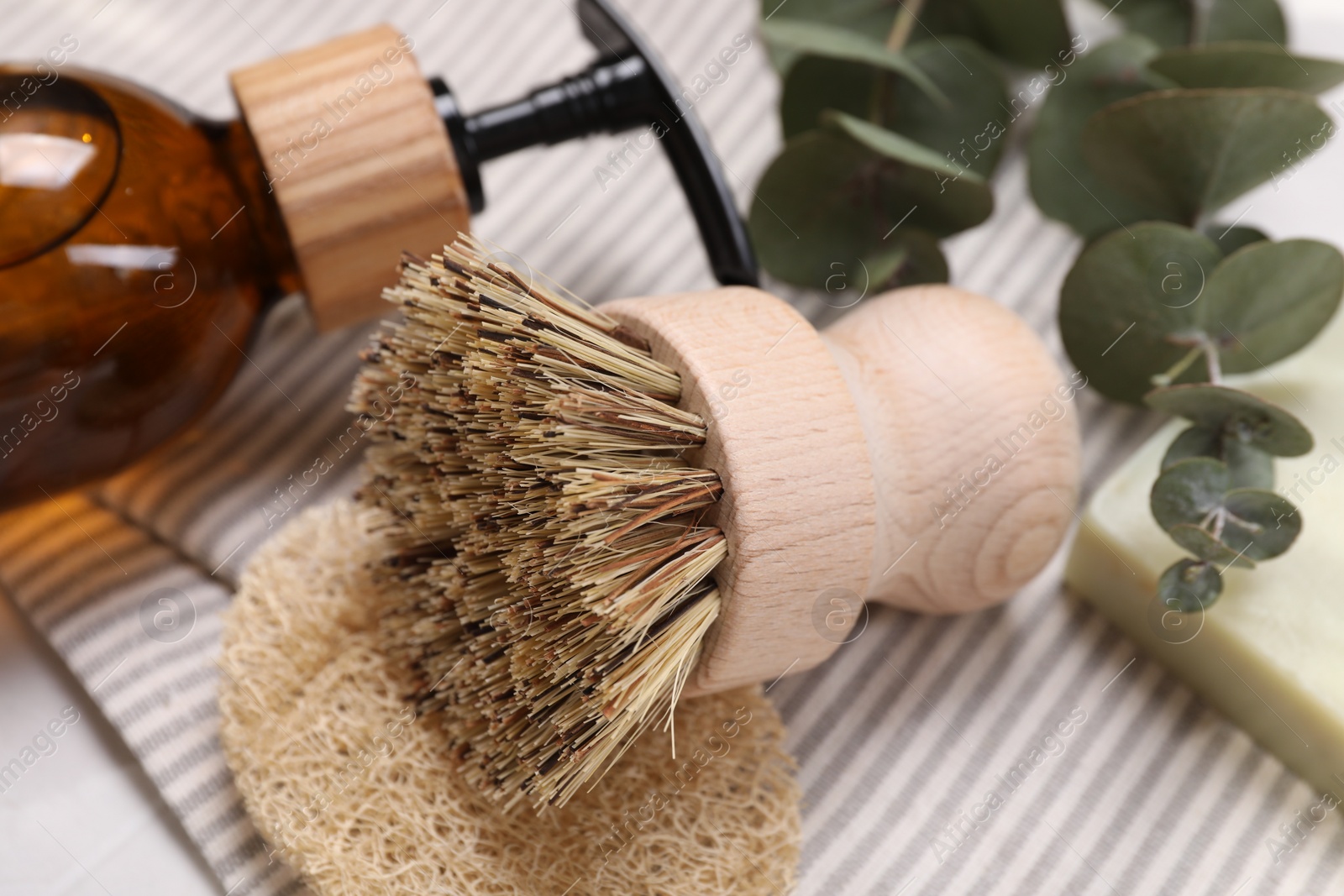 Photo of Cleaning brush, sponge, dispenser and eucalyptus leaves on table, closeup