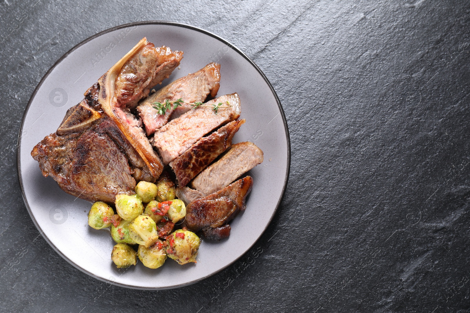 Photo of Delicious fried beef meat, vegetables and thyme on black table, top view. Space for text