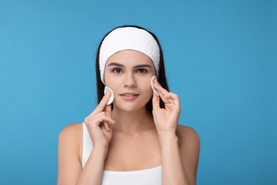 Photo of Young woman cleaning face with cotton pads on light blue background