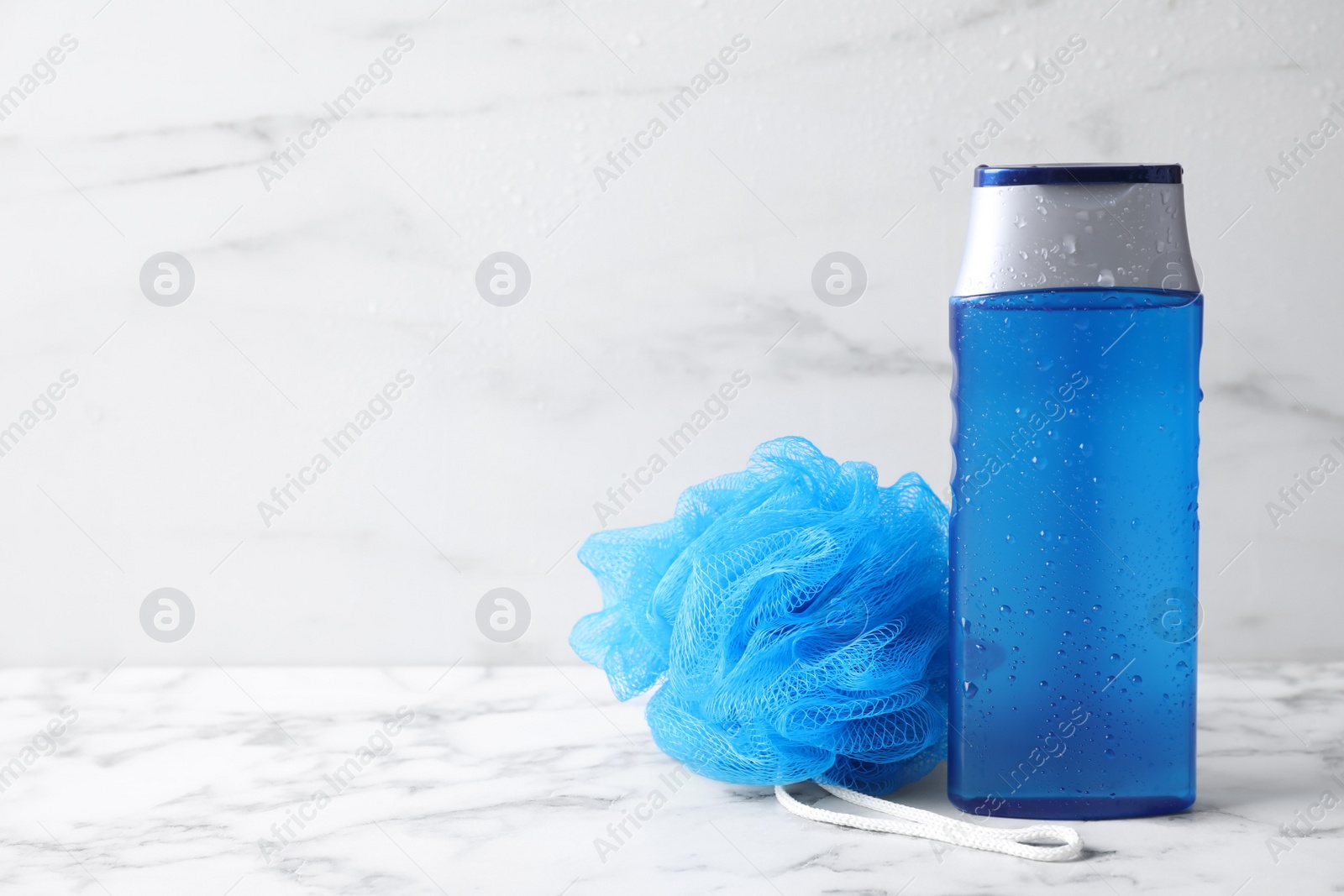 Photo of Bottle with water drops and bast wisp on white marble table, space for text. Men's cosmetics