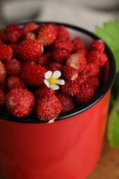 Fresh wild strawberries and flower in mug on table, closeup