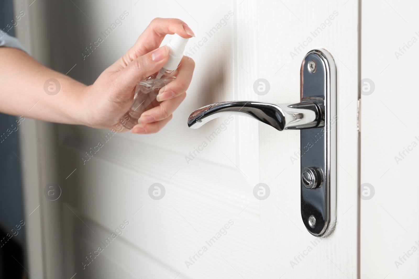 Photo of Woman spraying antiseptic onto door handle indoors, closeup