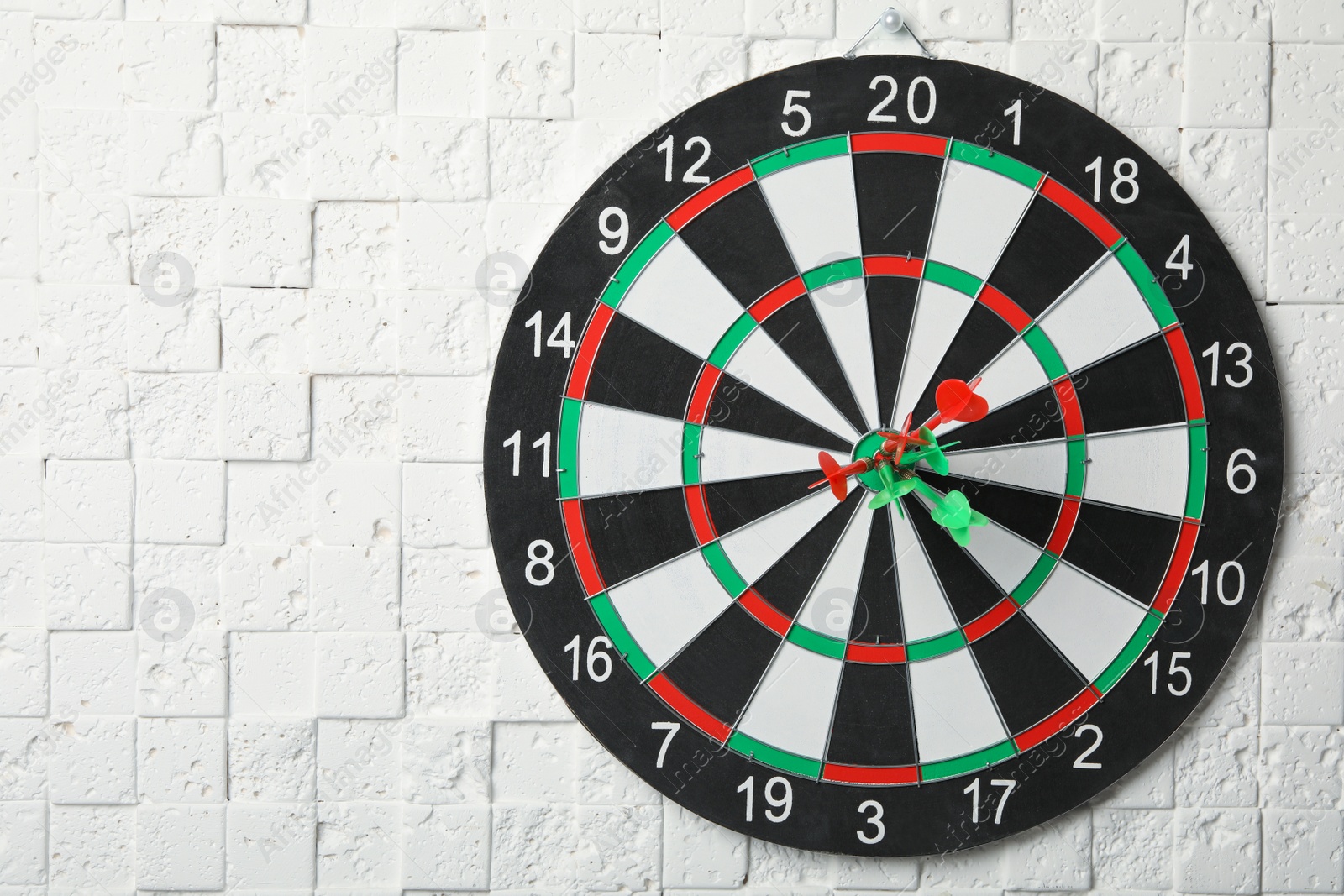 Photo of Dart board with arrows hitting target on white textured wall. Space for text