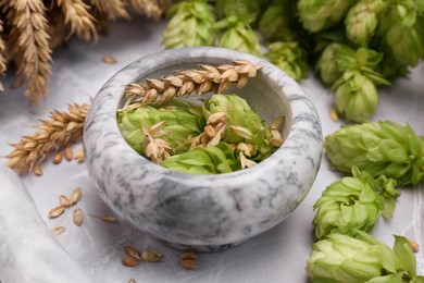Photo of Mortar, fresh hops and ears of wheat on light grey marble table, closeup