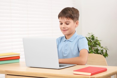 Photo of Boy using laptop at desk in room. Home workplace