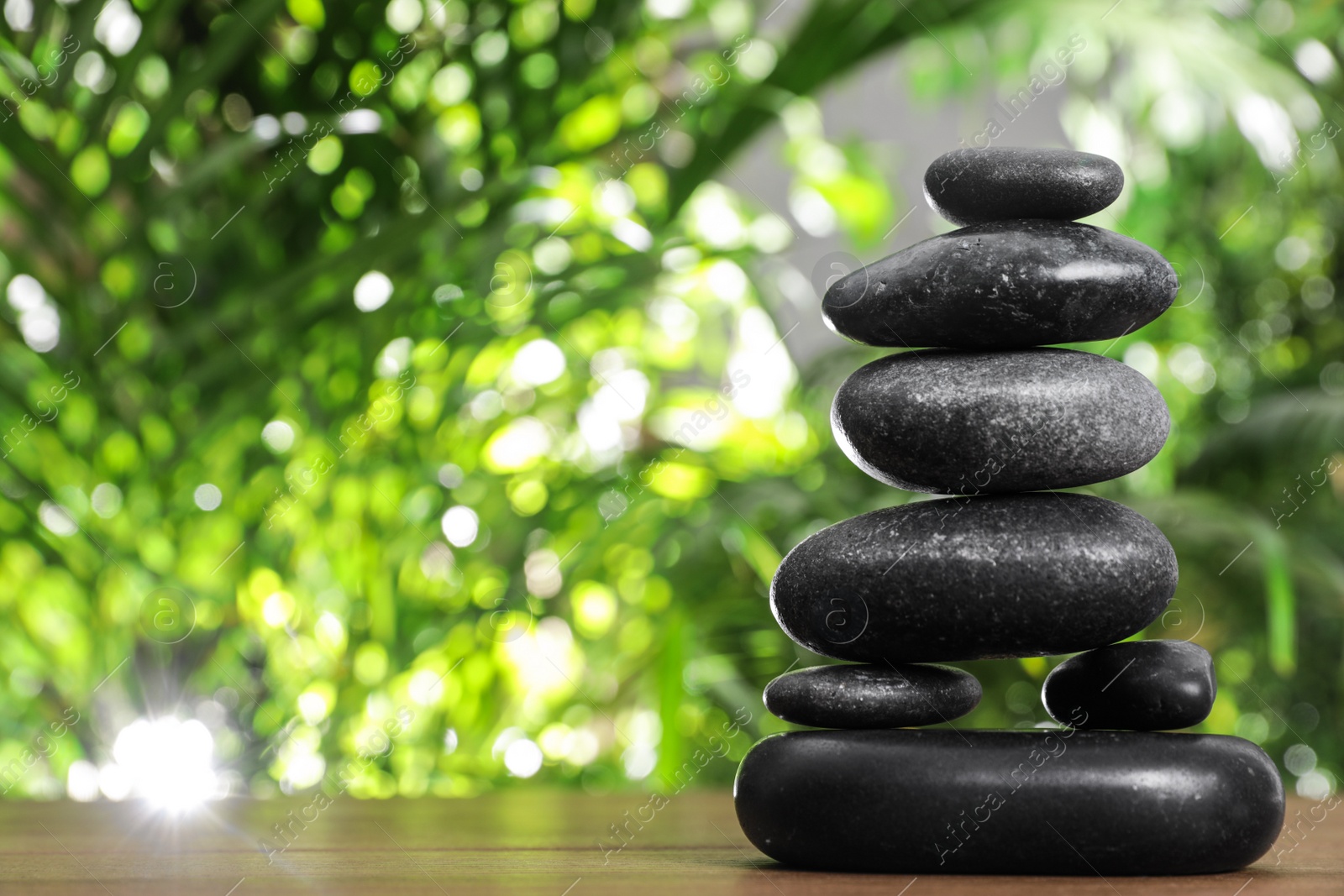 Photo of Table with stack of stones and blurred green leaves on background, space for text. Zen concept