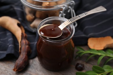 Photo of Jar of tasty tamarind sauce, spoon and fresh pods on wooden table