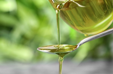 Pouring hemp oil into spoon on blurred background, closeup