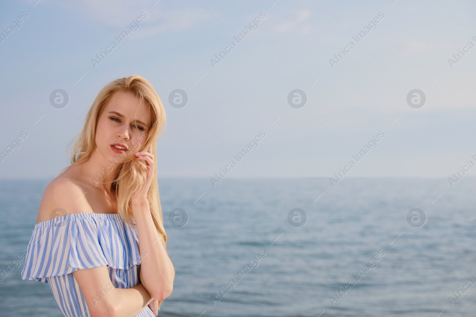 Photo of Beautiful young woman near sea on sunny day, space for text