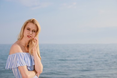 Beautiful young woman near sea on sunny day, space for text