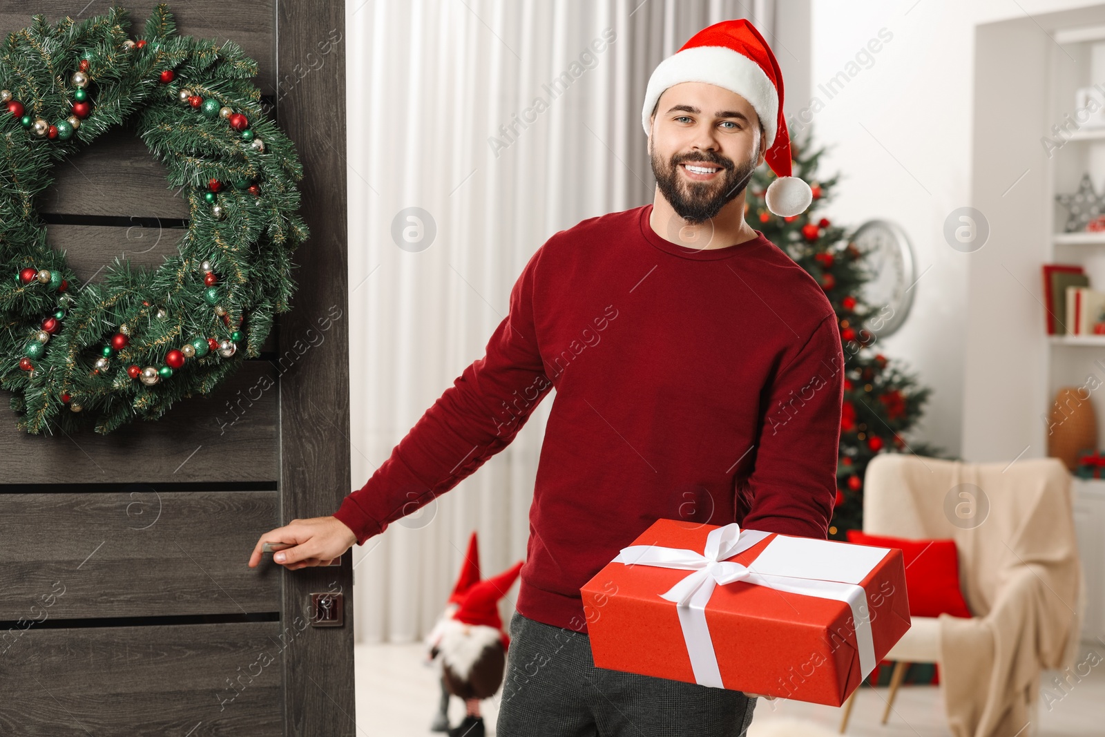 Photo of Young man in Santa hat with Christmas gift box received by mail indoors