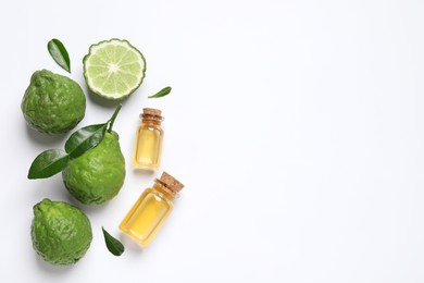 Photo of Glass bottles of bergamot essential oil and fresh fruits on white background, flat lay. Space for text