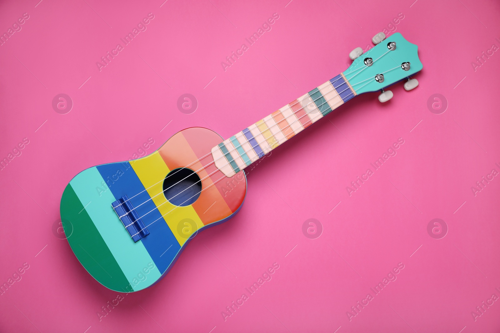 Photo of Colorful ukulele on pink background, top view. String musical instrument