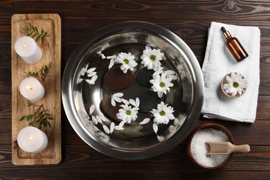 Photo of Bowl with water, flowers, stones and burning candles on wooden floor, flat lay. Pedicure procedure