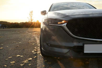 Photo of Black modern car parked on road at sunset, closeup. Space for text