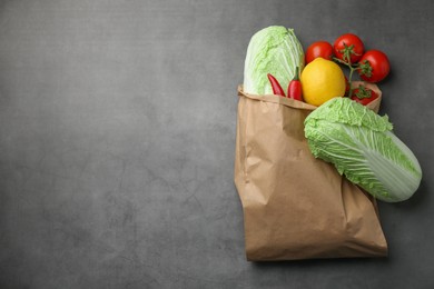 Photo of Paper bag with fresh Chinese cabbages, lemon, tomatoes and chili pepper on grey textured table, top view. Space for text