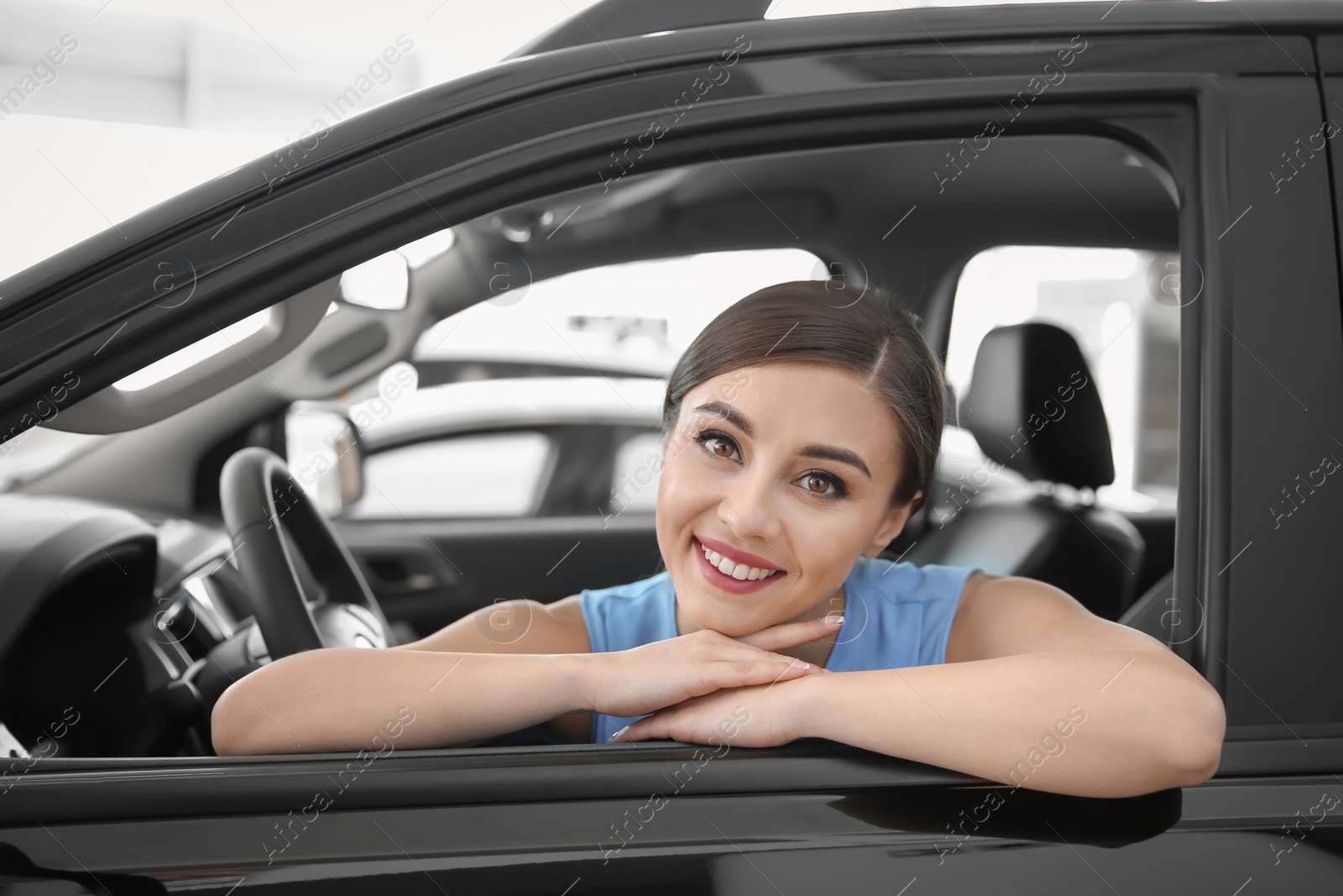 Photo of Young woman sitting in driver's seat of new car at salon