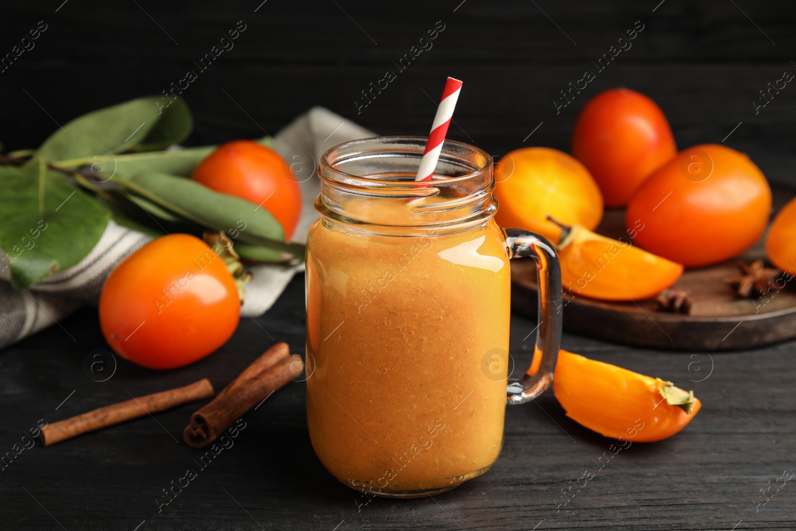 Photo of Tasty persimmon smoothie with straw on black wooden table