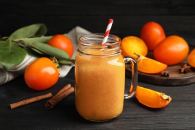 Tasty persimmon smoothie with straw on black wooden table