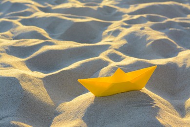 Photo of Beautiful yellow paper boat on sand outdoors, space for text
