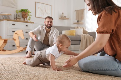 Photo of Happy parents helping their baby to crawl on floor at home