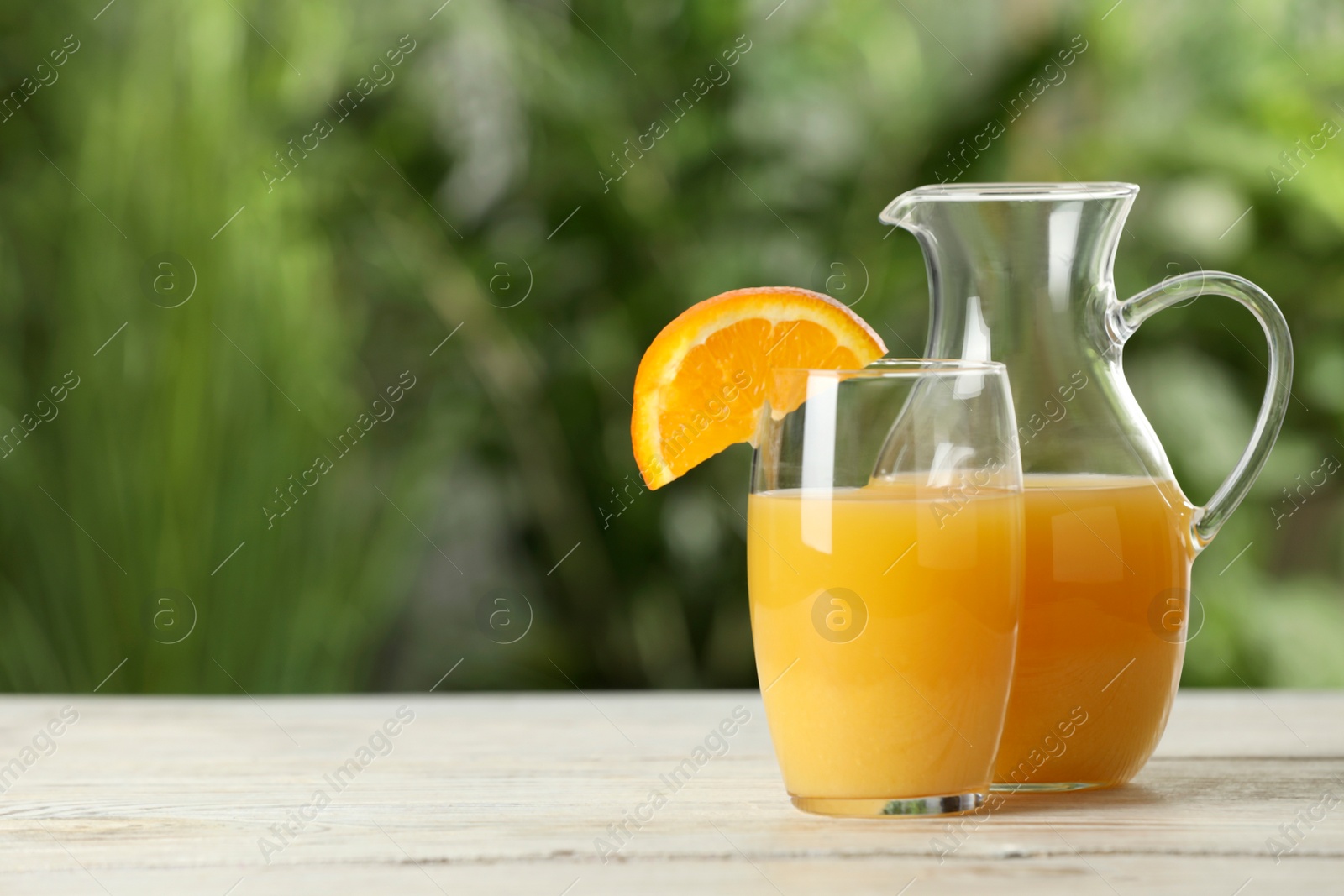 Photo of Tasty orange juice in glass and jug on white wooden table against blurred background. Space for text