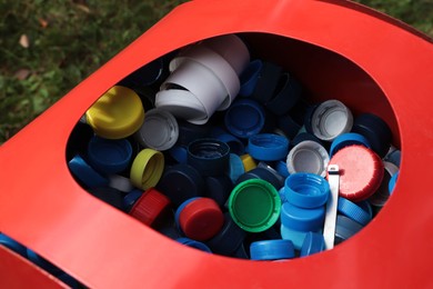 Different colorful bottle caps in red bin. Plastic recycling