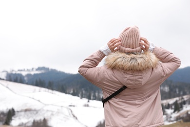 Photo of Young woman in warm clothes near snowy hill, space for text. Winter vacation