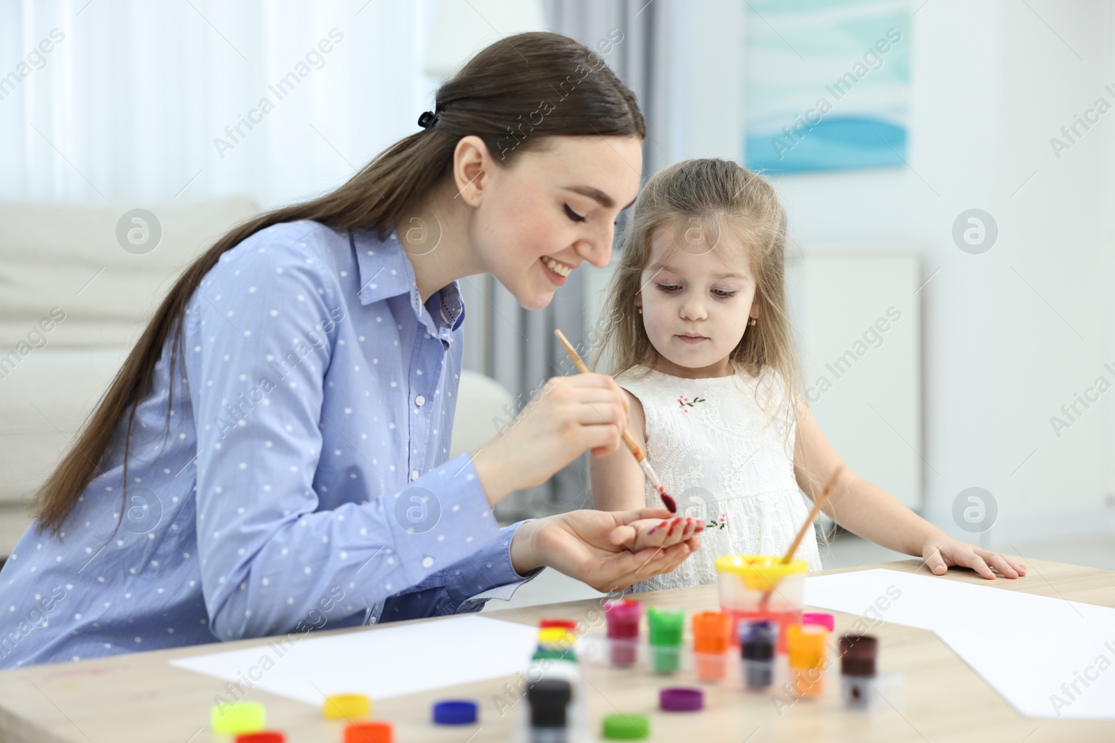 Photo of Mother and her little daughter painting with palms at home