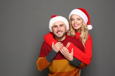 Photo of Young couple in Santa hats on grey background. Christmas celebration