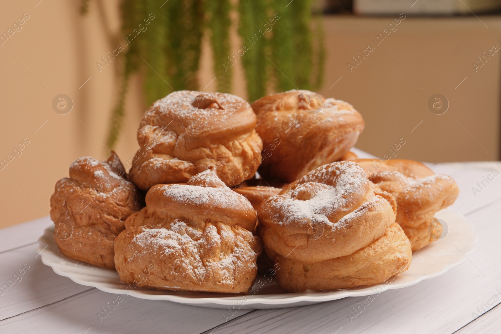 Photo of Delicious profiteroles with powdered sugar on white wooden table