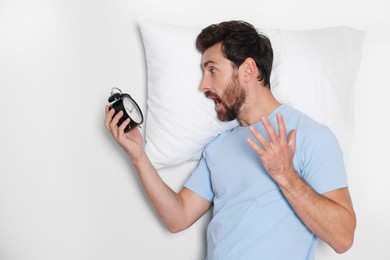 Photo of Emotional overslept man with alarm clock and pillow on light grey background