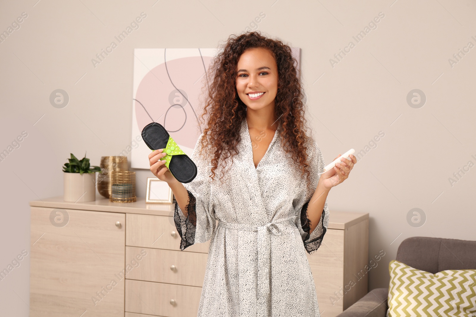 Photo of Young African American woman with reusable menstrual pad and tampon at home