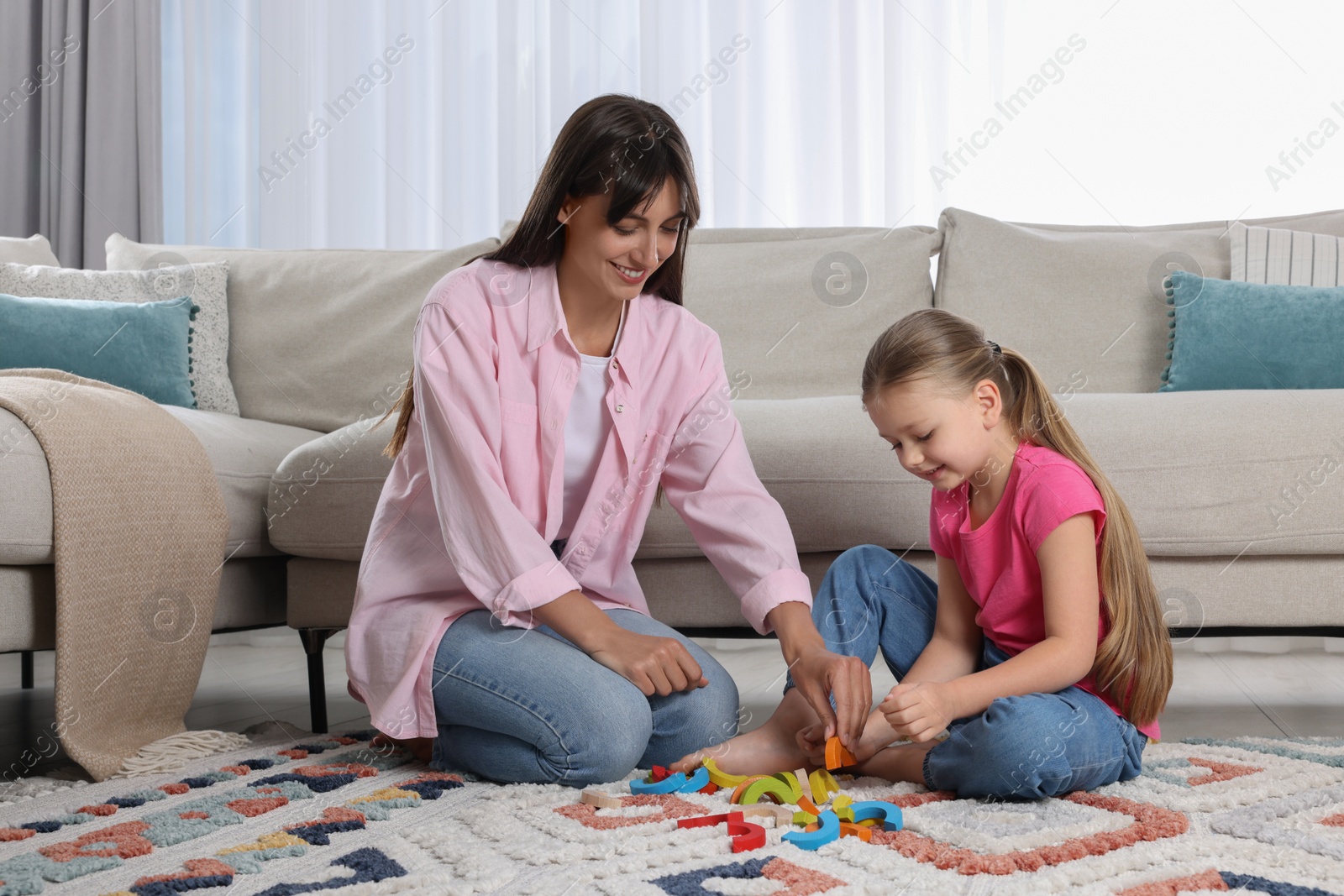 Photo of Motor skills development. Mother helping her daughter to play with colorful wooden arcs at home